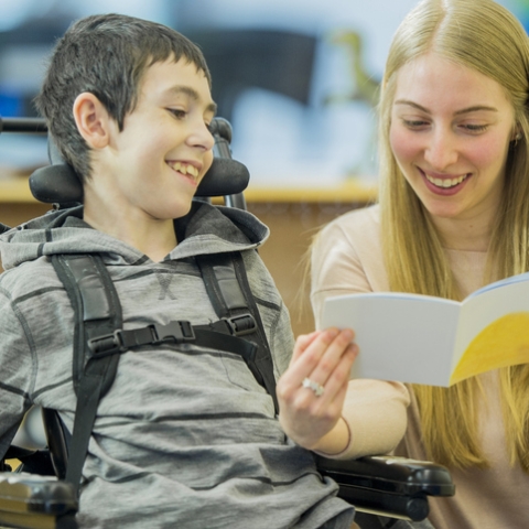 Child in wheelchair smiling with person with long blonde hair smiling and talking