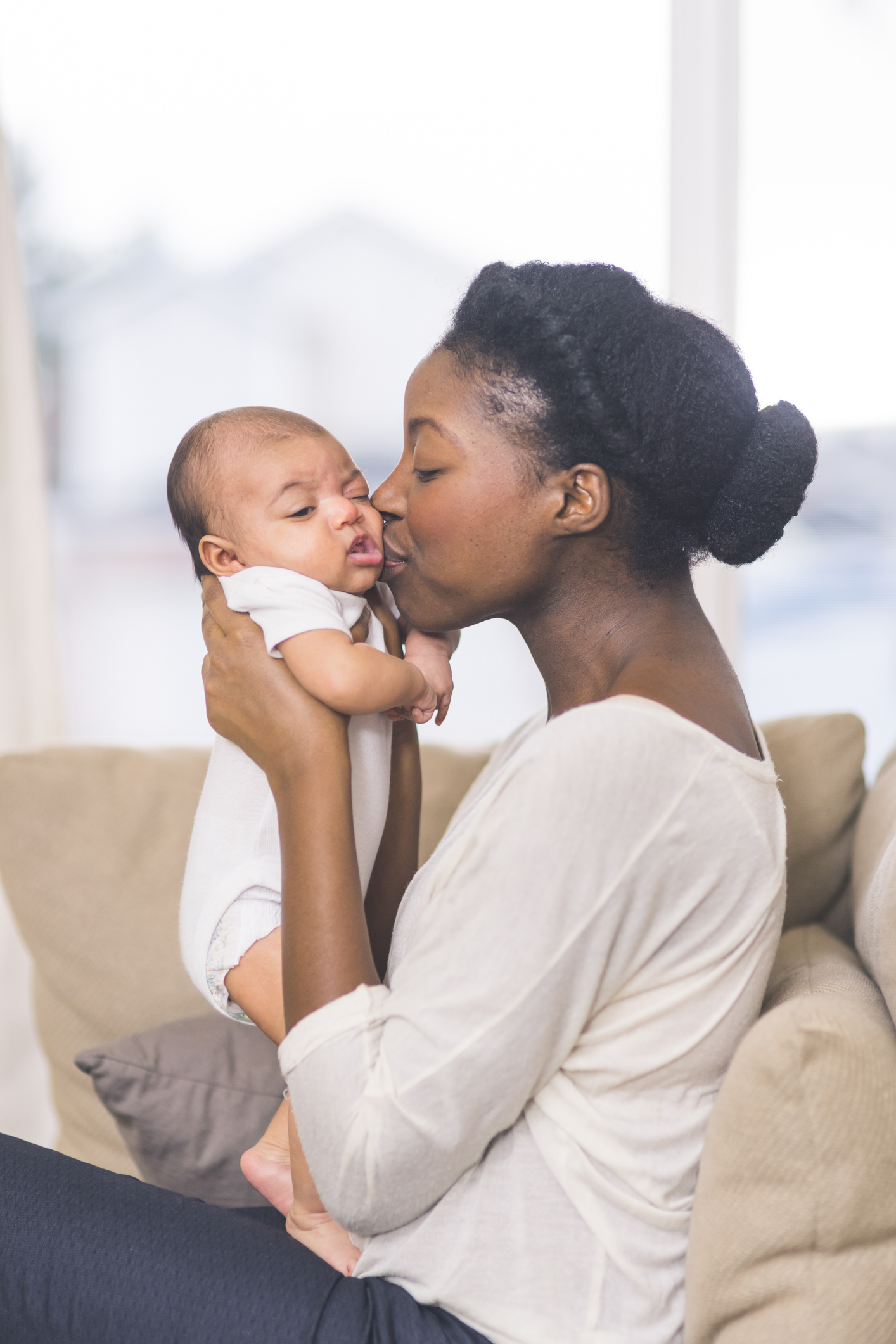 Black mother holding up baby and kissing them on the cheek