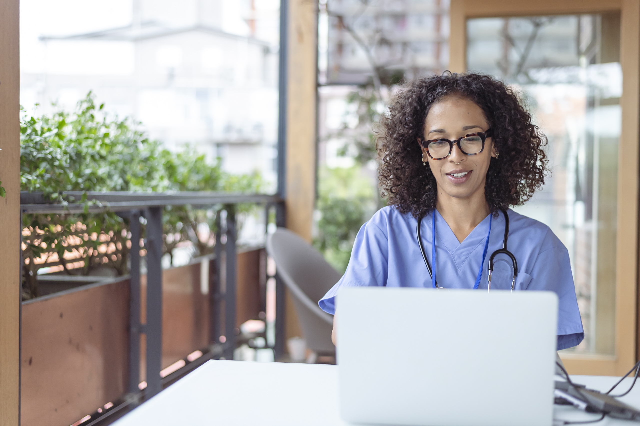 Black person with shoulder length curly hair wearing scrubs using a laptop
