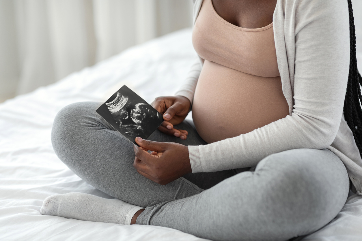 Black pregnant person holding belly with sonogram