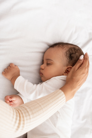 Arm stroking hair of sleeping baby on white surface