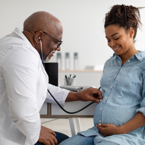 Black pregnant person smiling with Black bald male doctor