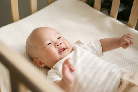 Asian baby laying on back in crib looking up smiling 