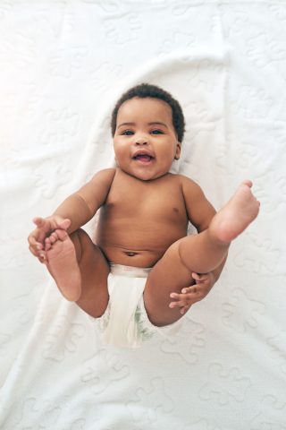 Black baby laying on back, smiling at camera with feet in the air