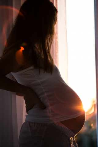 Pregnant person with long blond hair looking out the window turned to the side