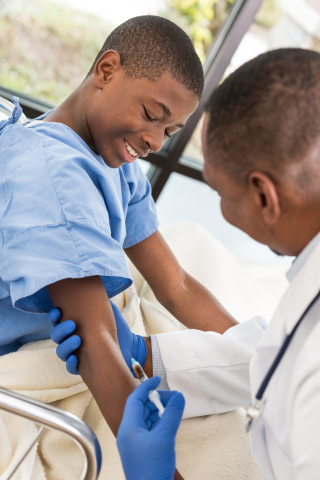 Black boy smiling while Black male doctor give shim a shot in doctors office