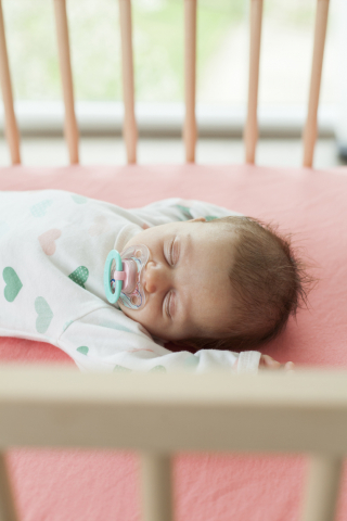Sleeping baby with dark brown hair in crib with coral lining
